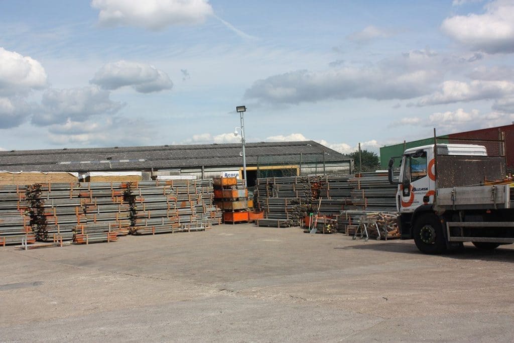 An Alltask truck next to piles of scaffolding material. 